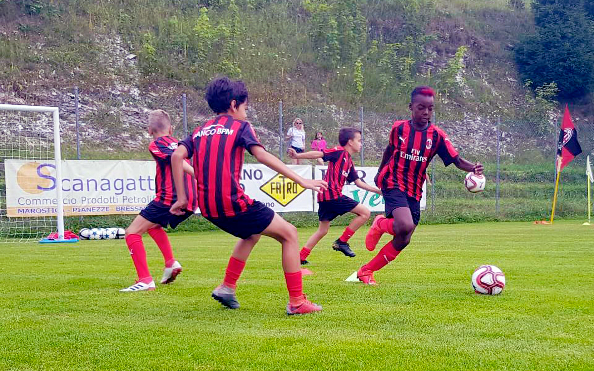 Jugadores jóvenes (tres contra dos) durante el entrenamiento táctico en los campamentos de fútbol de verano del AC Milán